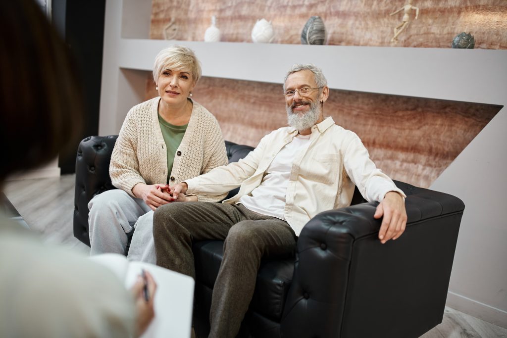 happy middle aged couple sitting on couch together near family counselor, relationship support
